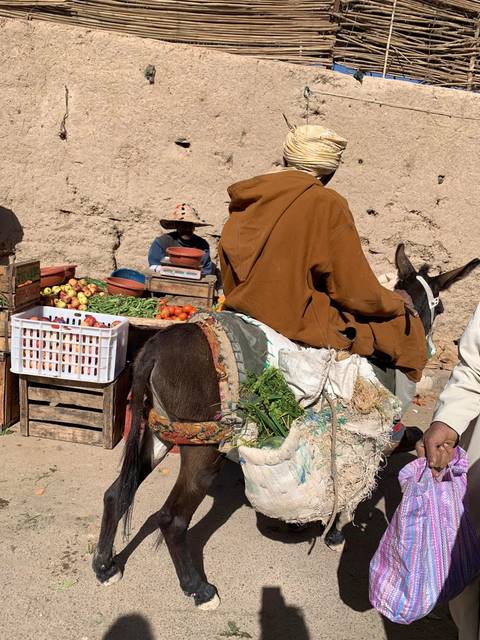 Man sitting on a donkey at a market with goods and produce.