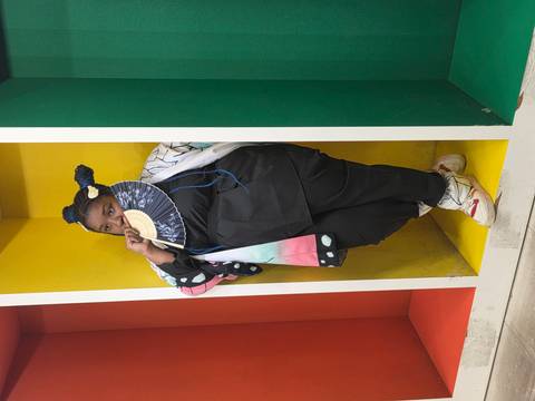 Person posing with a fan in a colorful setting.