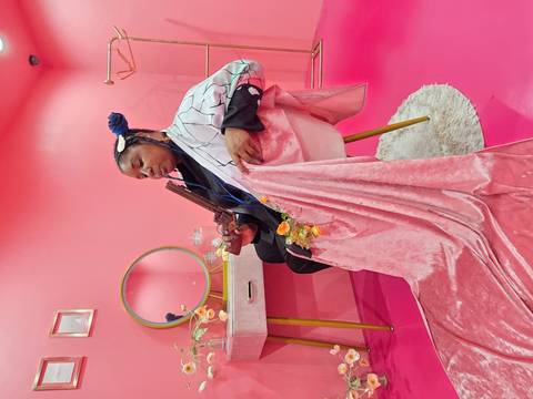 Person sitting in a pink-themed room with props.