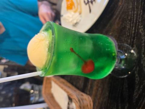 Green ice cream soda with a cherry and ice cream on top.