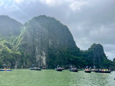       Tourists on boats surrounded by towering limestone cliffs.
  