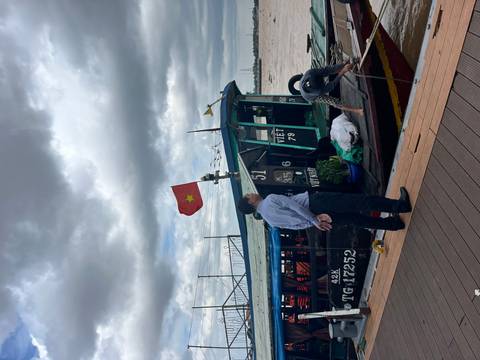       Boat on brown river with Vietnamese flag and cloudy sky.
  
