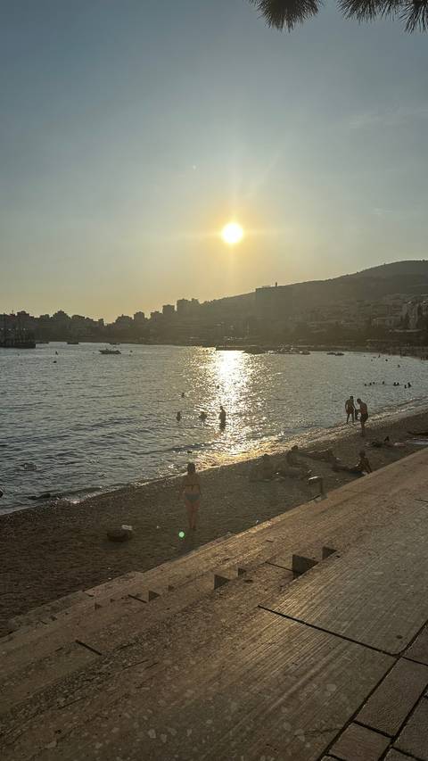 Beach scene at sunset with people swimming and relaxing.