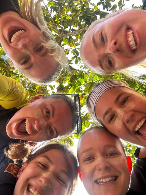 Five people looking down into the camera with greenery in the background.