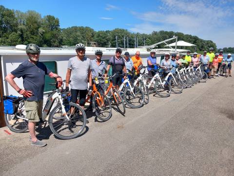 Group of cyclists posing with their bikes and a boat.