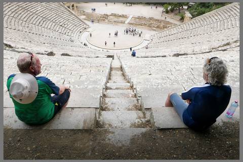 Two men sitting on the steps of an ancient amphitheater looking at the stage.