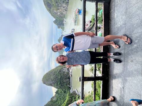       A couple posing on a balcony overlooking limestone karst hills and a calm bay.
  