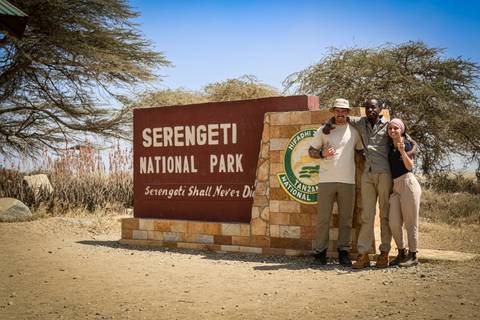 Three people posing by the Serengeti National Park entrance sign.