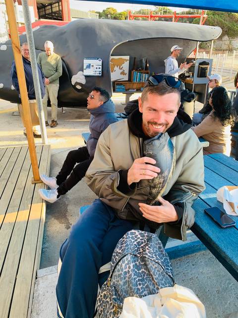 Man holding a fish at a bustling outdoor market.