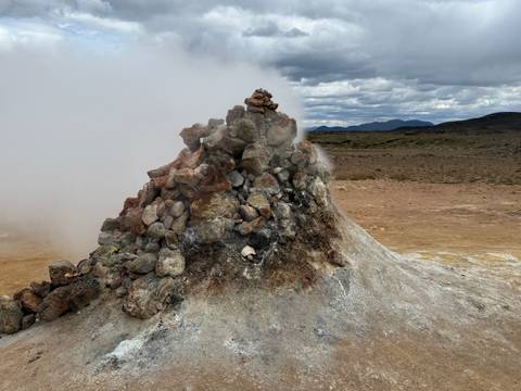 Steaming geothermal area with rocky terrain.
