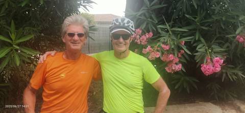 Two men in cycling gear posing with flowers.