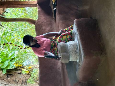 A woman sitting and using a traditional tool inside a rustic structure.