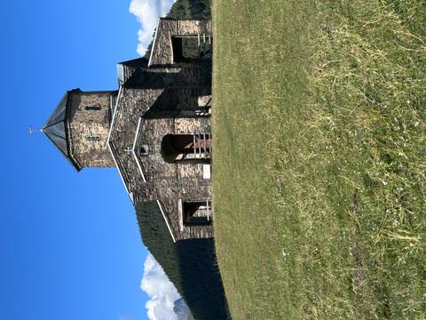       Stone church on a grassy hill under a clear blue sky.
  