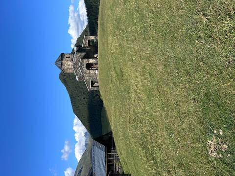       Stone church on a grassy hill with forested mountains.
  