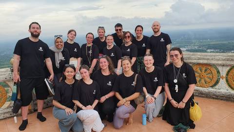       Group of tourists in matching shirts posing on a terrace.
  