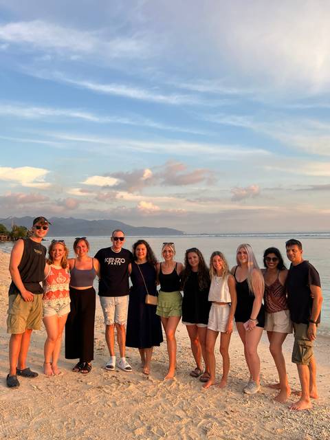       Group of friends smiling in front of a beach and setting sun.
  