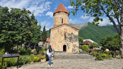       Woman standing in front of a historic church with mountains in the background.
  