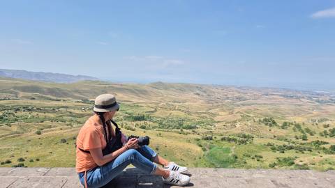       Woman sitting and enjoying a panoramic view of a landscape.
  