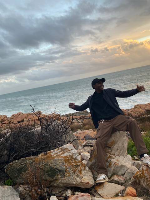 Two people posing by the waterfront with boats in the background.