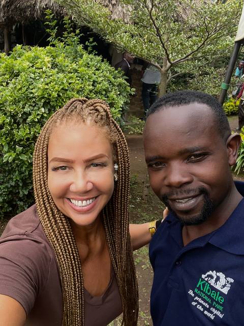       Two people smiling for a photo outdoors with greenery behind.
  