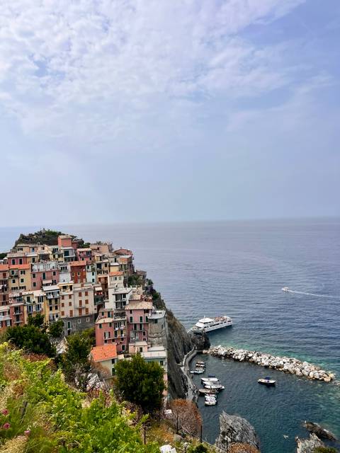 Houses perched on a cliff overlooking the sea with a boat in the water.