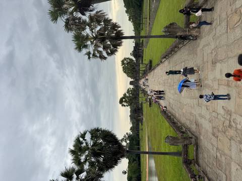 Tourists walking on a pathway towards a temple with palm trees.