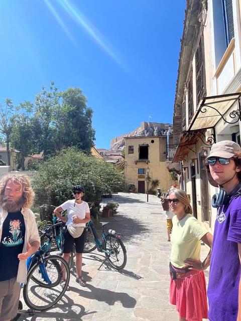       Group of people in a sunny, historic square with ancient buildings.
  