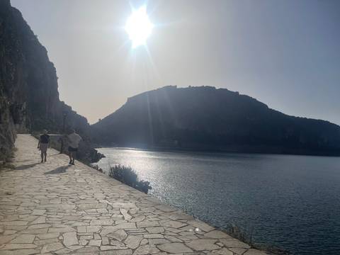       People walking along a coastline under a bright sun.
  