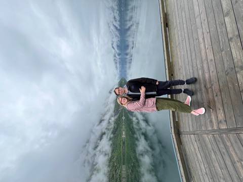       Couple standing on a pier with mountains in the background.
  