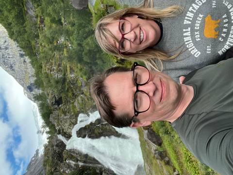       Couple taking a selfie by a waterfall in a lush area.
  