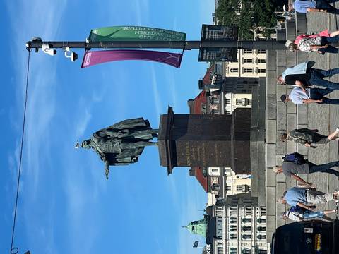       Statue of a historical figure with people walking nearby.
  