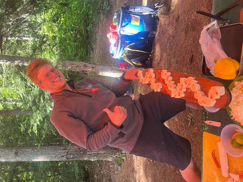       Person in outdoor setting presenting food with a thumbs-up.
  