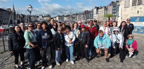 Tour group posing at a picturesque waterfront with historic buildings in the background.