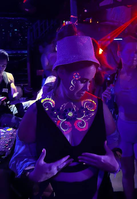       Person with colorful neon paint on skin, wearing a hat.
  