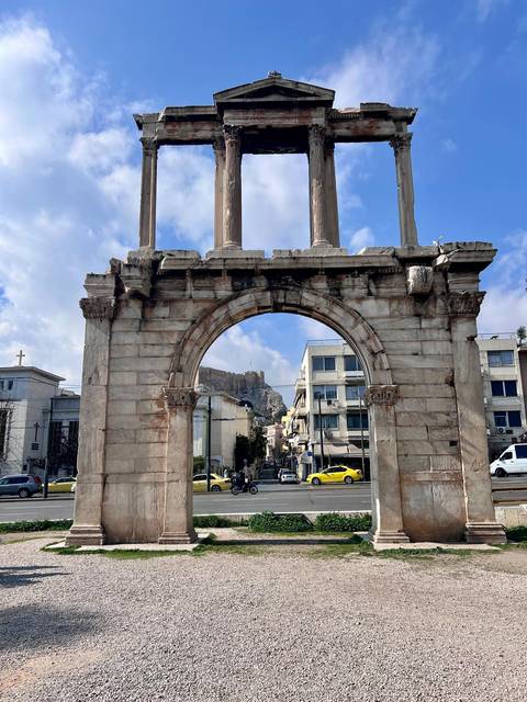 An ancient stone arch with a cityscape and Acropolis in the distance.