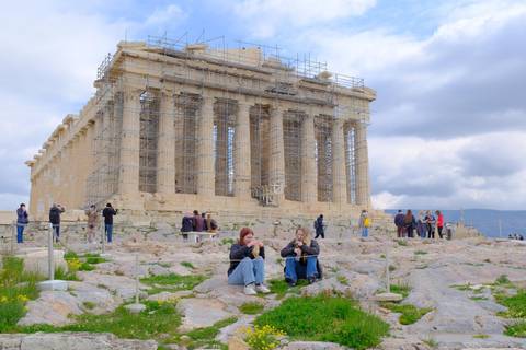 The Parthenon under reconstruction with people sitting nearby.