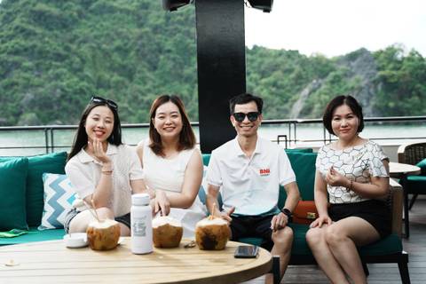 Four people sitting on a boat with coconuts, smiling.