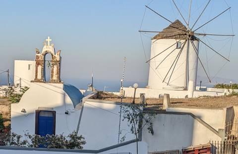 Traditional Greek architecture with a white windmill and a church bell tower.