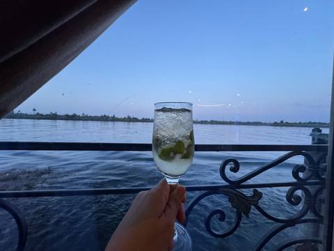       Hand holding a glass with a drink overlooking a river.
  