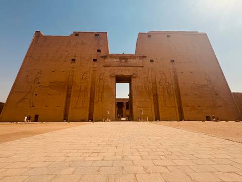       Large ancient temple facade with people and hieroglyphs.
  