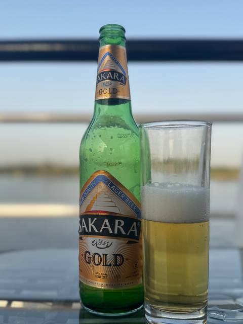       Bottle and glass of beer with an outdoor view.
  