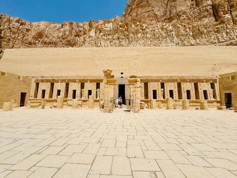       Entrance of an ancient temple with columns and a few visitors.
  