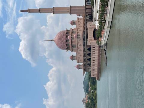 Pink mosque by the water under a blue sky with clouds.