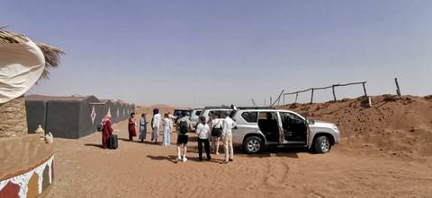 People standing near off-road vehicles in the desert camp.
