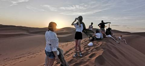 Group sitting on a dune with the sunset in the background.