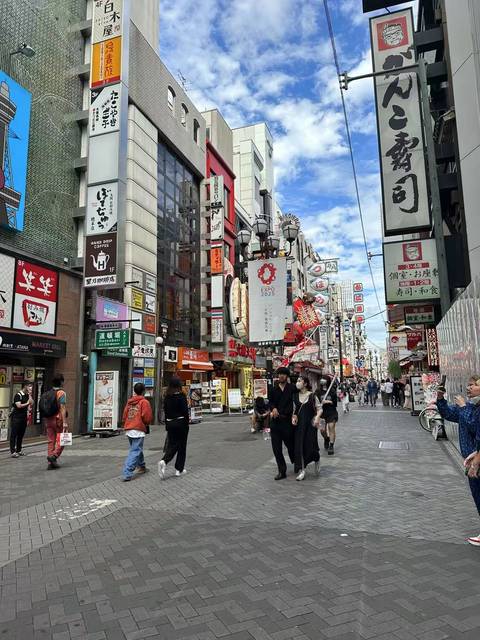 A bustling shopping street with people walking and various signs in Japanese.