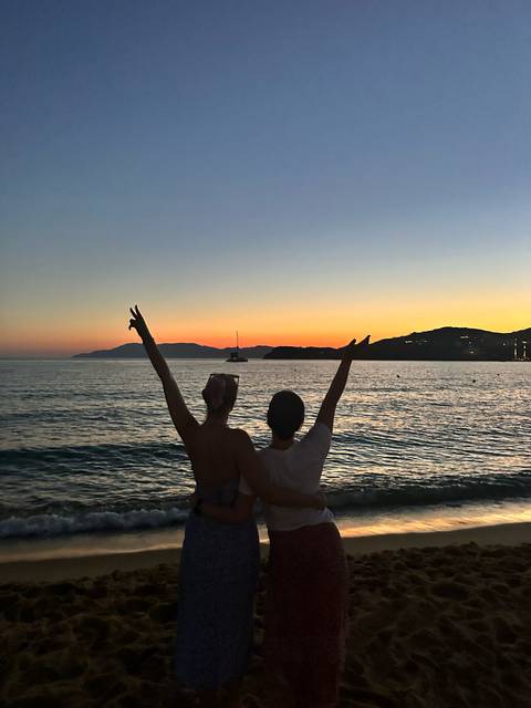Two people on a beach at sunset making peace signs.