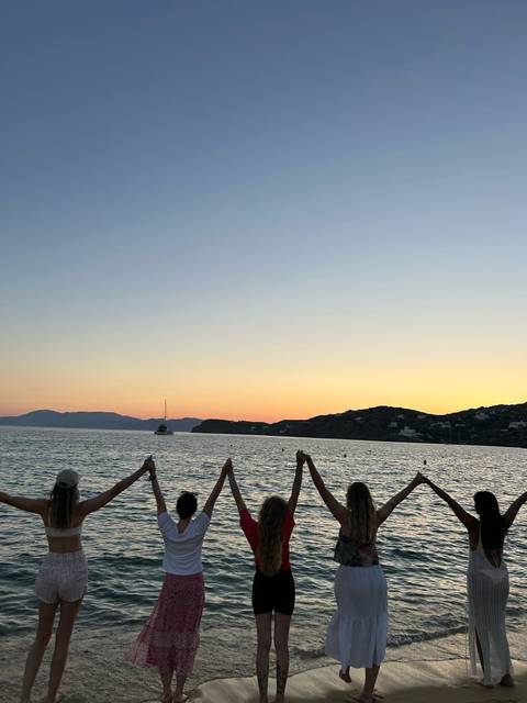 Four people on a beach holding their hands up at sunset.