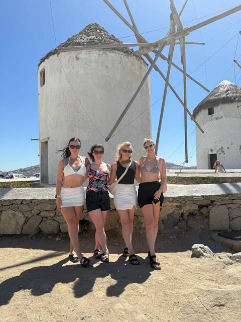 Four women posing on a sunny day in front of traditional windmills.