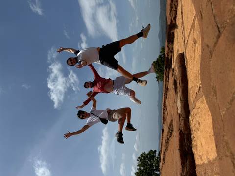       Three people jumping joyfully with a scenic view behind.
  